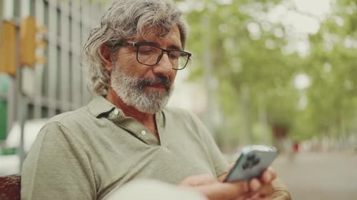 Man Typing on Phone on a Park Bench