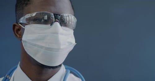 Closeup Slow Motion Portrait of African American Doctor in Face Mask and Glasses Turning to Camera