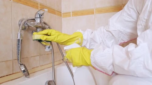 Person Cleaning Bathroom Faucet with Sponge and Spray