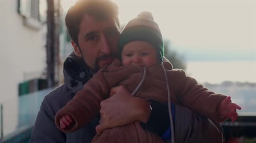 Man holding baby on bright day near apartments