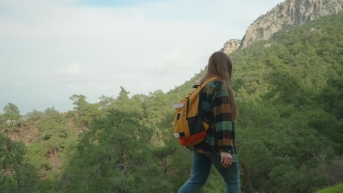 Solitary Woman in a Cozy Plaid Shirt and a Bright Backpack, She Ascends a Distant Mountain.