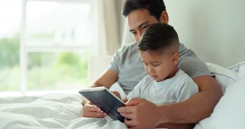 Father and Son Using Tablet Together in Bed