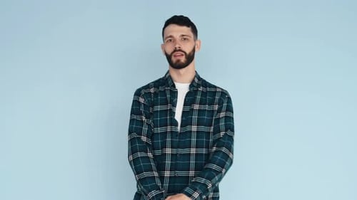 Against blue background. Man in casual clothes standing in the studio and showing emotions
