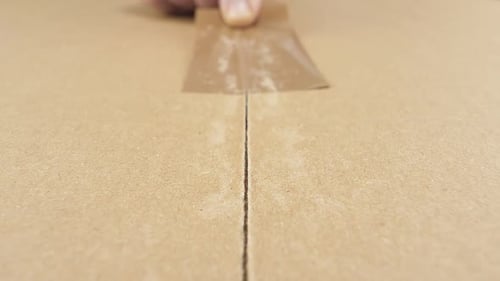 Hand Removing Tape to Open Cardboard Box