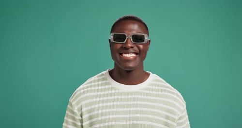 Fröhlicher, schwarzer Mann und Mode mit Sonnenbrille im Studio als Accessoire oder Beute auf grünem Hintergrund