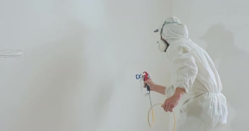 Adult Painting Wall with Paint Sprayer in Hazmat Suit