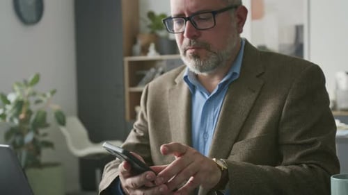 Businessman Using Laptop and Answering Phone Call in Office