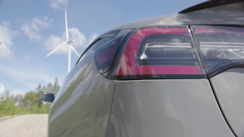 SLIDER - A generic electric vehicle is plugged in, wind turbine behind