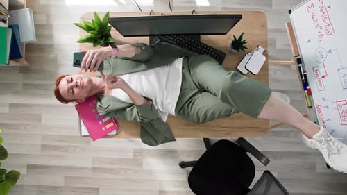 Relaxing Woman Lies on Desk, Using Cellphone