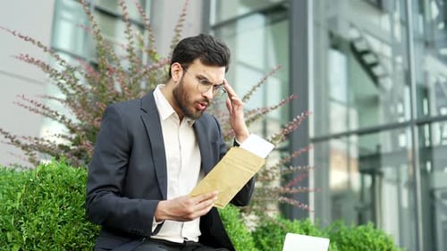 Disappointed businessman in a formal suit reading a letter with bad news on the street near business