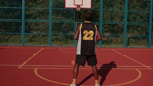 Front View of Fit African Man Wearing Sports Clothes Playing Street Basketball Alone Throwing Orange