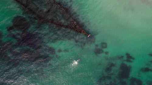 Aerial View of Swimmer Passing By an Ancient Shipwreck in Sunlit Clear Blue Waters