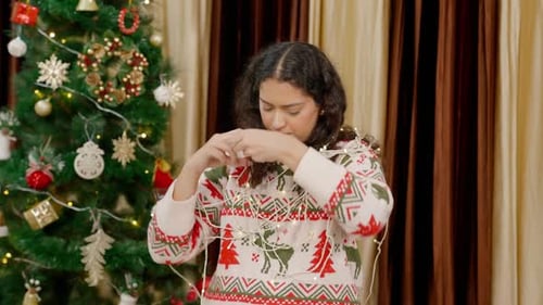 Indian Woman Untangling Herself from Fairy lights, Lights with Christmas Tree in background