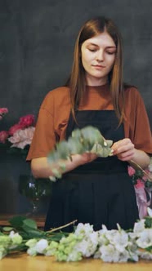 Young Woman Florist in a Flower Shop Prepares a Plant for a Beautiful Bouquet of Fresh Flowers