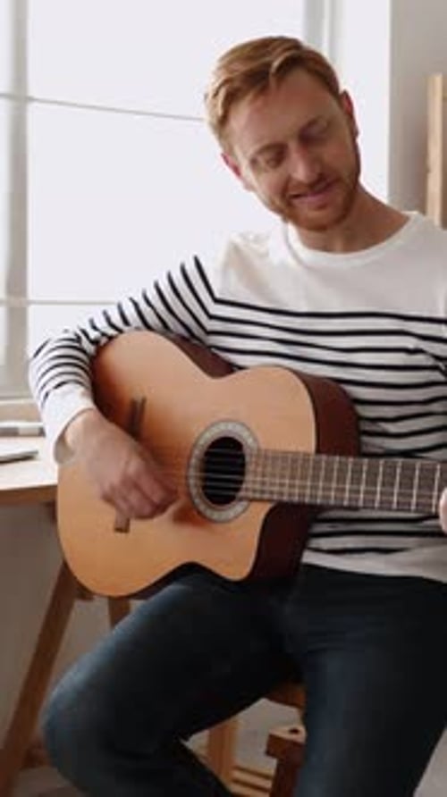 Man Plays Acoustic Guitar Indoors During the Day