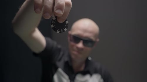 Homem deixa cair fichas na mesa de pôquer. Ação. Bandido com óculos deixa cair ficha sobre pilha de fichas
no pôquer