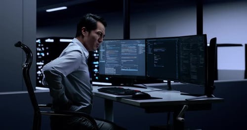 Side View Of Programmer Having A Backache While Writing Code By Desktops In The Server Room