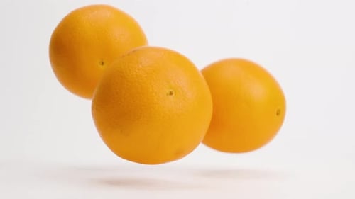 Leuchtend frische ganze Orangen fallen und hüpfen in Zeitlupe auf die weiße Tischplatte