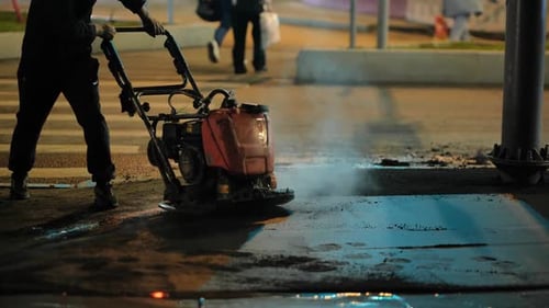 Worker Compacting Hot Asphalt on City Street at Night Repairing Road Surface