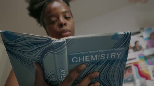 Focused Woman Studies Chemistry From Textbook Indoors