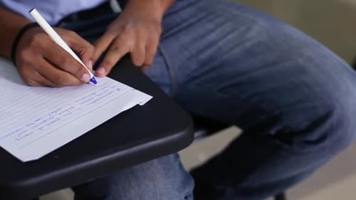 Vue rapprochée d'un garçon étudiant écrivant sur le papier de sa salle de classe, vêtu d'un pantalon en jean, A