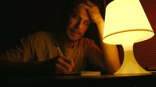 Stressed Exhausted Man Writing in a Notebook at Night