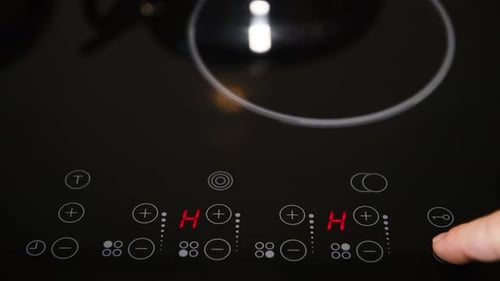 Close up of electric stove control panel, male finger pressing buttons, red LED indicators switched