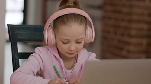 Focused girl doing homework with laptop and headphones
