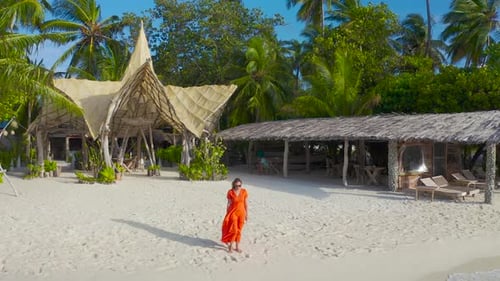 Beautiful Sexy Girl in a Red Dress Walking Down the White Sand Beach on a Paradise Tropical Island