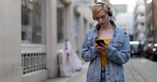 Woman with headphones uses mobile phone in city street