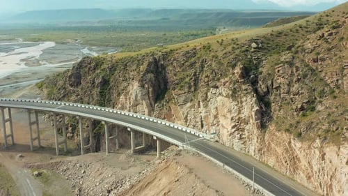 Aerial view flyover with modern highway bridge spanning across river capturing beautiful mountains