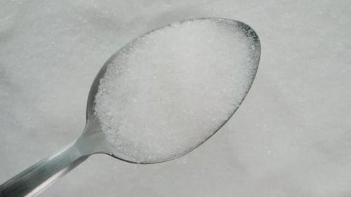 A Spoon of Sugar Slowly Rises Upward, with a Background of Rotating Sugar Below.