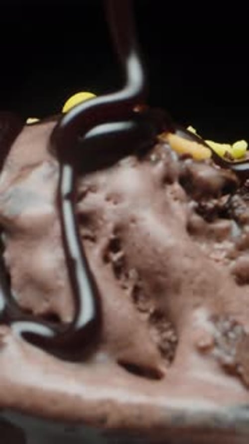 Balls of chocolate ice cream and sugar sprinkles rotate and I pour them with chocolate, close-up Ver