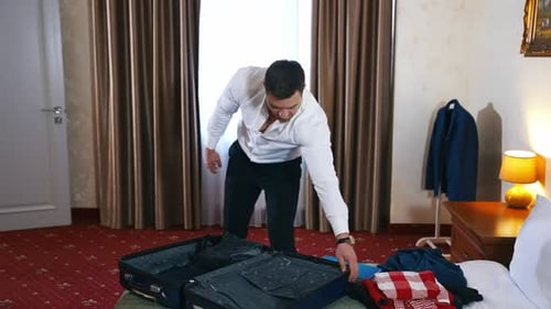 Arrival to a hotel. Handsome man unpacking the baggage and closing bag.