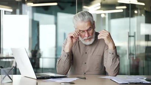 Senior Man Rubbing Eyes at Desk, Office Setting