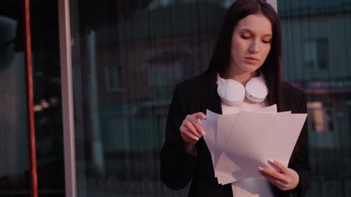 A businesswoman holds documents outdoors, portraying a freelancer, social media manager, or office
