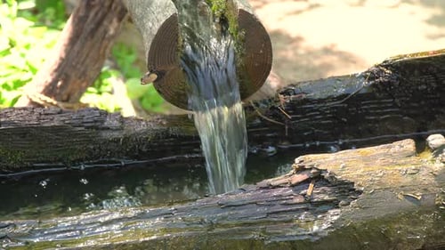 Wasser, das durch offene Holzrohre fließt und alte heruntergekommene hölzerne Wassermühle zum Mahlen von Weizen füllt und