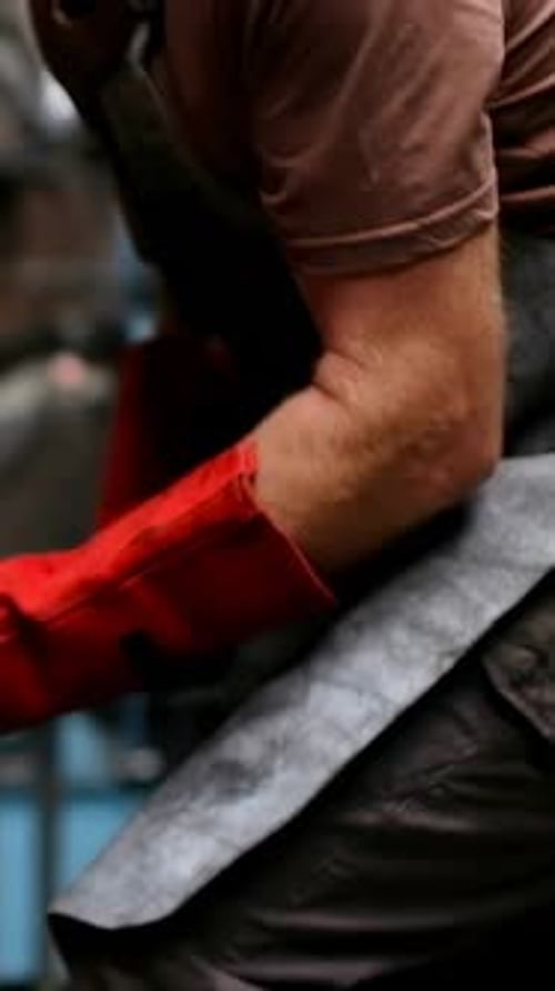 Vertical video: Responding to rod glowing, worker gripping and checking at forge, wearing apron
