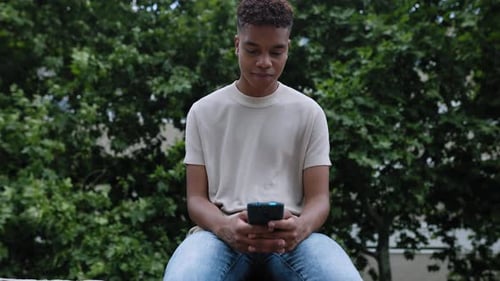 Young Man Smiling While Using Smartphone in Park