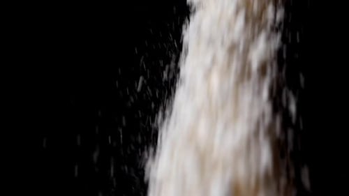 White flour falls down from above on black background.