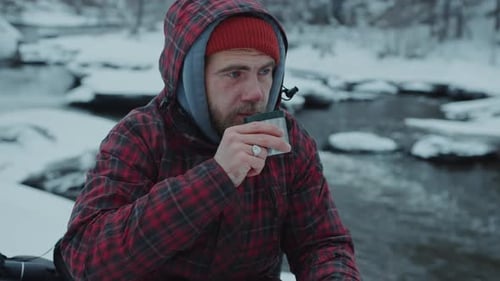 Man Drinks Hot Beverage by Frozen River in Winter