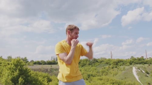 A Man Wearing a Yellow Shirt is Practicing His Boxing Techniques in a Picturesque Park with Lush