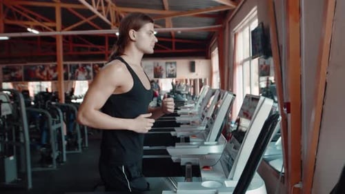 Portrait of a Longhair Man Jogging on Treadmill in Gym Side View Man Trains in Gym Doing Cardio
