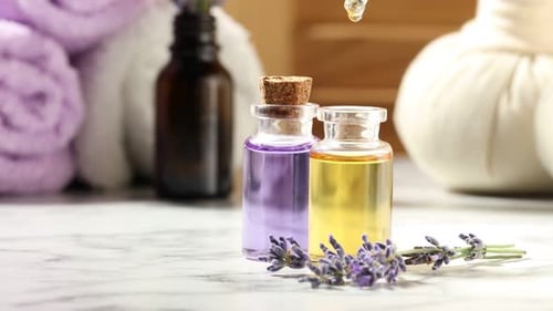 Dripping lavender essential oil into bottle at white marble table, closeup. Space for text