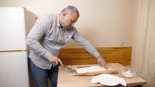 Man Cuts Dough on a Wooden Table