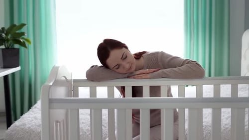 Woman Resting Head on Baby Crib at Home