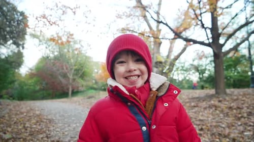 Statische Ansicht eines süßen kleinen Jungen, der lächelt und für ein Foto in roter Jacke auf dem Weg nebenan posiert