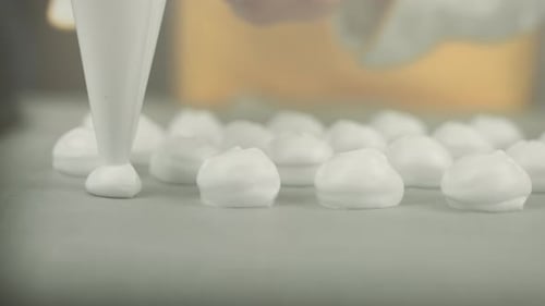 Close up of a whipped egg white cream being placed by a chef with a icing bag on a backing plate to