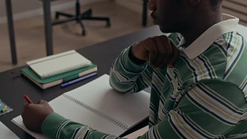 Estudiante masculino negro enfocado anotando en un cuaderno