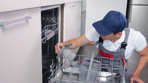 Männlicher Klempner inspiziert das zu reparierende Spülmaschinenteil in der Küche